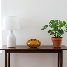 Load image into Gallery viewer, Computer-generated illustration: Sam Stang Augusta Studios amber ripple art glass piece on a wooden console table beside a white lamp and a potted plant