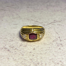 Load image into Gallery viewer, An 18 karat gold ring with a red gemstone center and two smaller diamonds set in gold bands on a textured surface.

